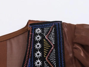 Vue macro des broderies géométriques colorées sur l'encolure de la robe en mousseline