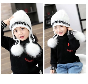 Dettaglio del cappello in maglia bianca con paraorecchie, motivo pied-de-poule e pompon