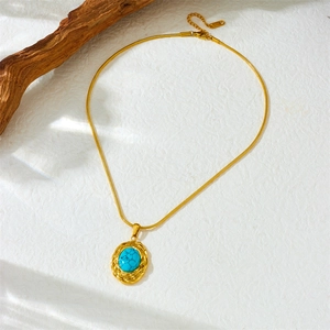 Gold stainless steel snake chain necklace with oval turquoise pendant on textured background