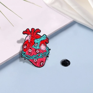 Artistic anatomical heart enamel pin with eye patterns and green thorns on blue background