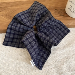 Close-up of checkered fabric hair scrunchie with handmade tag on a textured surface