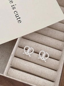 Close-up of heart-shaped twisted silver stud earrings on a beige jewelry tray