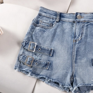 Detailed close-up of light blue denim shorts with side buckles and frayed raw hem