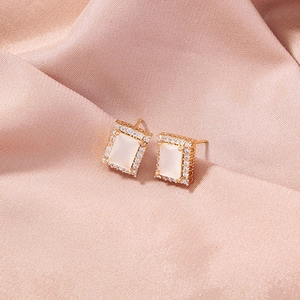 Macro shot of gold four-leaf clover earrings with zircon and opal inlays on pink satin
