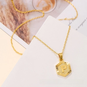 Close-up of gold hexagonal pendant with embossed letter P on a delicate chain