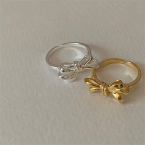 Detail of bow-shaped open rings in gold and silver finish on a textured background