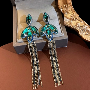 Detail of luxury emerald leaf tassel earrings on jewelry box with golden frame