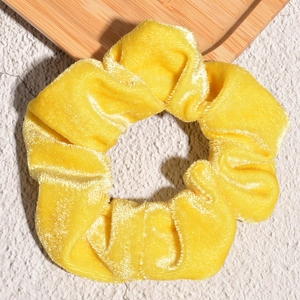 Detailed view of yellow velvet scrunchie showing soft fabric texture and pleated design
