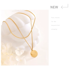 Detail of double-layered gold necklace with coin pendants on a minimalist white base