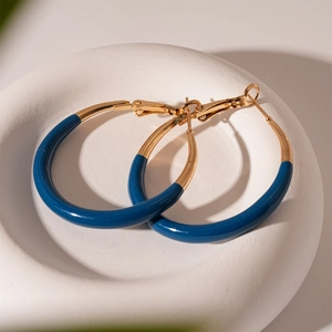 Detail of blue and gold geometric hoop earrings on white stone tray with soft shadows
