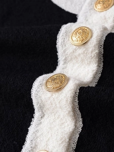 Macro detail of black tweed fabric with white wavy trim and embossed gold vintage buttons