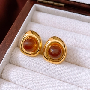 Detailed macro view of gold-tone irregular round resin earrings in a wooden jewelry box