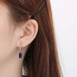 Gros plan d'une boucle d'oreille rectangle en zircon bleu avec anneau torsadé argenté