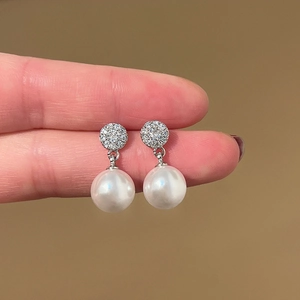 Macro shot of silver pearl drop earrings with sparkling zircon studs on a brown background