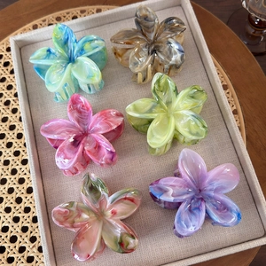 Detail of six marble-patterned frangipani flower hair claws in various vibrant gradients