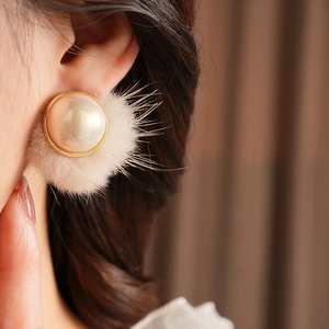 Detail of cream plush fur pearl earring with gold trim on model for autumn winter style