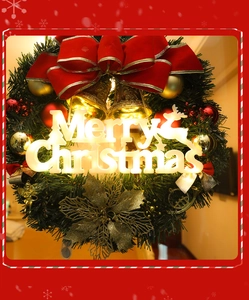 Detail of a lighted Christmas wreath with a red bow, golden bells, and Merry Christmas sign