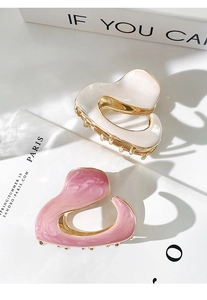 Close-up of pink and white pearlescent heart hair claws on a gold metal base
