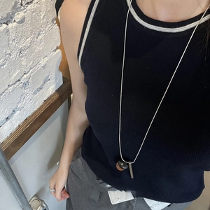 Detail view of long acorn necklace with wooden pendant and metal bar on black tank top