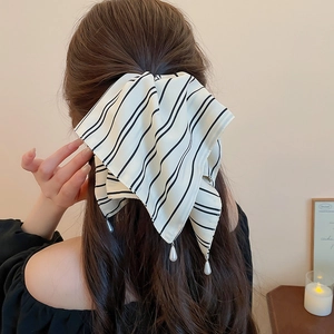 Détail de pince à cheveux avec nœud en tissu rayé et perle sur une coiffure élégante
