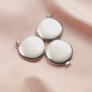 Three silver round stainless steel locket pendants on pink cloth with polished finish