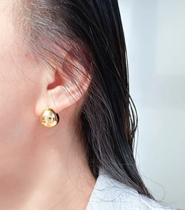 Close-up of golden teardrop stud earrings worn on the ear showing polished finish