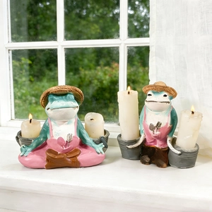 Detailed view of hand-painted meditating frog candle holders on a sunny windowsill