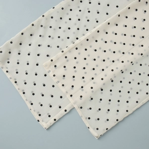 Detailed macro view of white chiffon fabric with black polka dots and fine stitched edges