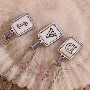 Detail of rectangular titanium steel pendants with white mother of pearl inlay and letters