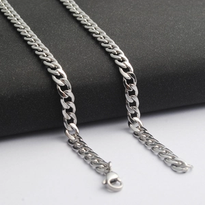 Polished silver stainless steel Cuban link necklace with secure clasp on textured surface