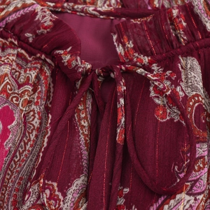 Vue macro du tissu à motif paisley avec fils dorés sur une robe rouge foncé