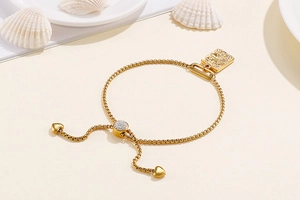 Detail of adjustable gold box chain bracelet with square charm and heart pendants