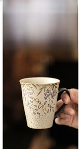 Macro shot of hand-painted wisteria and gold-rimmed ceramic mug with flint red glaze