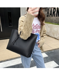 Close-up of black lychee grain leather tote bag with stylish tassel detail on model