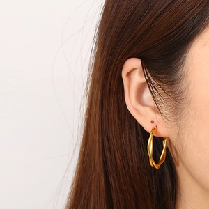 Detail of twisted rope gold hoop earrings worn by a model against a white background