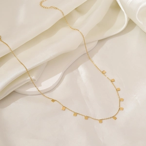 Close-up of a gold geometric butterfly necklace resting on white silk fabric folds