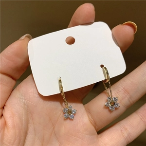 Detailed close-up of gold floral earrings with zircon stones on a white display card