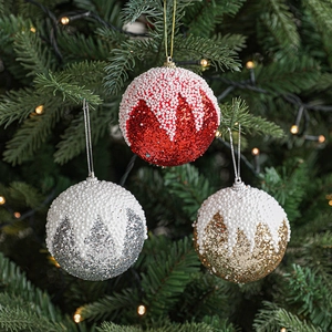 Trois boules de Noël en rouge, or et argent avec effet neige sur sapin festif