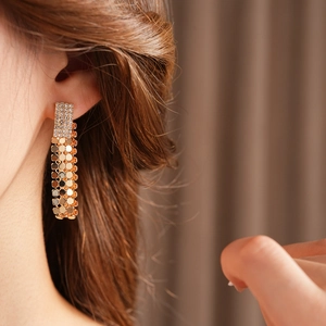 Dettaglio di orecchini pendenti geometrici dorati con strass indossati da una modella