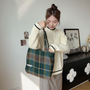 Detail of green plaid wool tote bag showing the texture and brand label in home setting