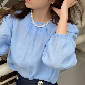Close-up of elegant pearl necklace paired with a blue puff sleeve top and pearl earrings