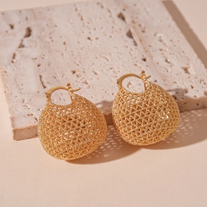 Vintage gold hollow woven ball earrings with matte geometric mesh texture on marble