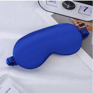 Close-up of blue satin sleep mask with elastic strap on comfortable bedroom setting