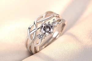 Macro shot of silver woven couple ring with three sparkling round zircons on beige fabric