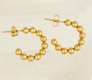 Detailed close-up of 18K gold beaded C-shape earrings on a neutral beige background