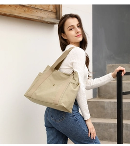 Model wearing a large beige canvas tote bag with side pocket and comfortable wide straps