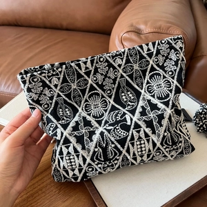Detailed close-up of ethnic white floral embroidery on a black linen cosmetic bag