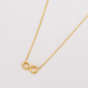 Vue macro du pendentif infini doré avec cristaux pavés sur une fine chaîne croisée