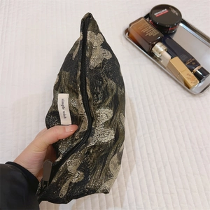Detailaufnahme der goldenen Schmetterlingsstickerei auf schwarzer Vintage-Kosmetiktasche