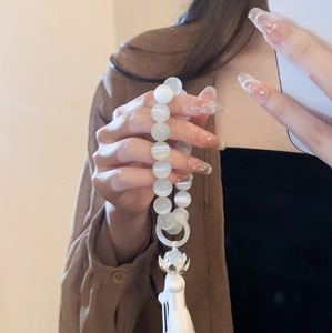Close-up of white cat eye stone bead bracelet with silver lotus flower and silk tassel
